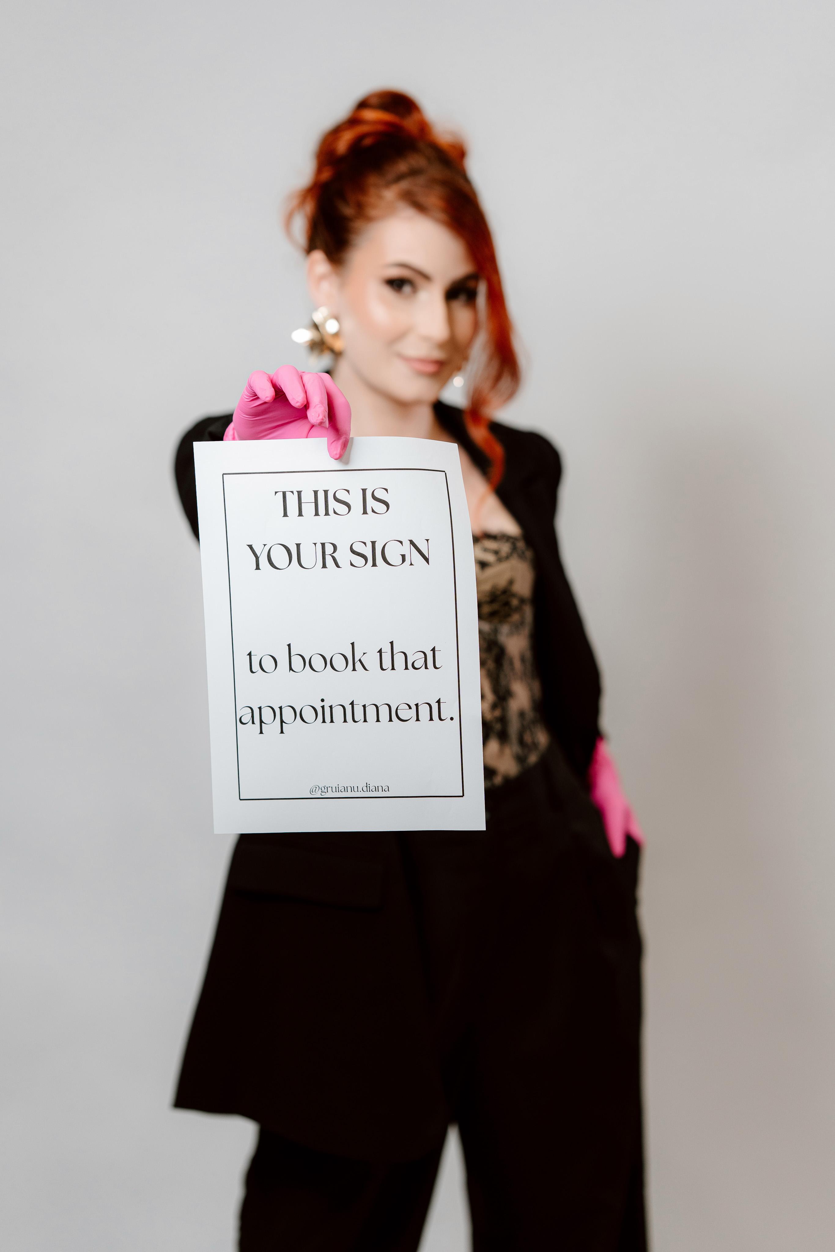 Diana Gruianu cu mănuși roz, ținând un afiș "This is your sign to book that appointment"